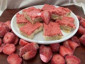 A white plate topped with strawberry shortcake next to sliced strawberries.